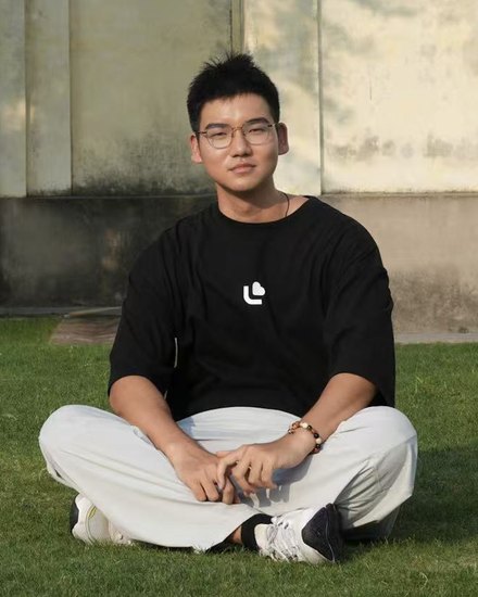 Tongle Shen, sitting cross-legged on grass.